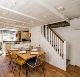 A dining area with a wooden table and six chairs next to a staircase and an open kitchen with a door leading outside at Sea Horses in Port Isaac