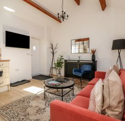 A living room with a red sofa a black round coffee table a blue chair and a wall mounted tv at Guillemot in Flamborough