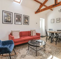 A living room with a red sofa blue rocking chair round glass coffee table and dining table with black chairs at Guillemot in Flamborough