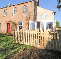 A two-story brick house with white windows a red door a glass porch and a wooden fence in a garden at Hillside Hideaway in Wigton