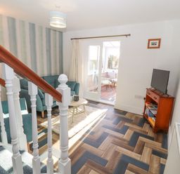 A living room with teal armchairs a small round table a television on a wooden stand and a sliding glass door leading to a sunroom at Hillside Hideaway in Wigton