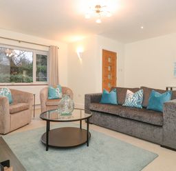 A living room with a gray sofa and two beige armchairs around a glass coffee table at Tandarra in Keswick