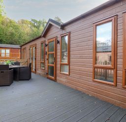 A wooden deck outside a brown cabin with outdoor dining furniture at Snuggledown Troutbeck 5 White Cross Bay near Windermere