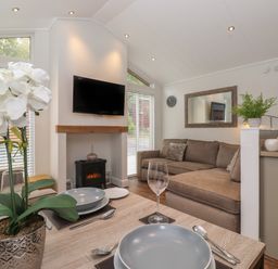 A dining table set with plates and glasses near a living room with a brown sofa a wall-mounted TV and a small fireplace at Snuggledown Troutbeck 5 White Cross Bay near Windermere