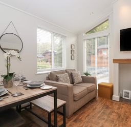 A dining table set with plates and glasses next to a sofa and a wall-mounted TV at Snuggledown in Troutbeck 5 White Cross Bay near Windermere