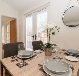 A dining table set with plates glasses and cutlery with a plant on it in a room with a round mirror at Snuggledown Troutbeck 5 White Cross Bay near Windermere