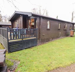 A wooden cabin with a fenced deck and plastic chairs on a grass lawn at Latrigg Lodge Number 9 Burnside Park near Keswick