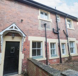 The exterior of a brick house with a black door and multiple windows with cream-colored frames at Courtyard Cottage in Alnwick