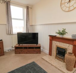 A living room with a television on a wooden stand and a fireplace with decorations at Courtyard Cottage in Alnwick