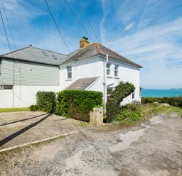 A white two-story house with hedges and a gravel driveway near the sea at Tamarama House in Port Isaac