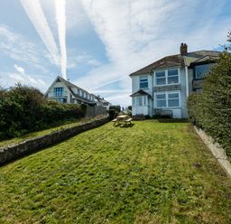 A grassy backyard with a wooden picnic table and bench behind a two-story house at Tamarama House in Port Isaac