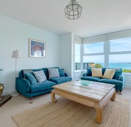 A living room with two blue sofas a wooden coffee table a fireplace and large windows with ocean view at Tamarama House in Port Isaac