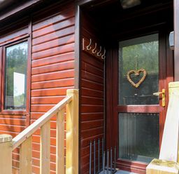 Entrance door with a heart-shaped decoration on the glass of a wooden cabin with railing at Hill Lodge Applethwaite 2 Limefitt Park near Windermere