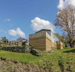 An elevated mobile home with wooden fencing and stone retaining walls on a grassy slope with a tree nearby at 11A Mansion View in Cove near Kilcreggan