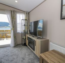 A living room with a television on a cabinet next to a glass door and window with outdoor seating visible at 11A Mansion View in Cove near Kilcreggan