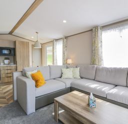 A living room with a grey sectional sofa and wooden coffee table next to an open kitchen area at 11A Mansion View in Cove near Kilcreggan