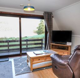 A living room with a leather armchair wooden coffee table television and large sliding glass doors at 27 Invergarry Lodges South Laggan near Invergarry