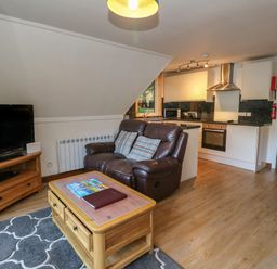 A living room with a leather sofa a wooden coffee table a television and an open kitchen at 27 Invergarry Lodges South Laggan near Invergarry