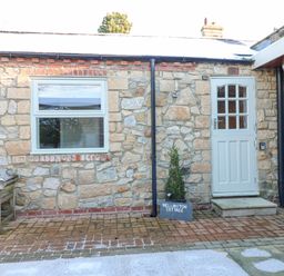 A stone exterior wall with a window and a white door and a wooden bench at Wellington Lodge Cottage in Middleton Tyas