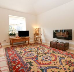 A living room with a patterned rug sofa table with a TV and flowers wooden chair and wall-mounted television at Wellington Lodge Cottage in Middleton Tyas