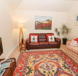 A living room with two sofas a colorful rug a floor lamp paintings and a plant at Wellington Lodge Cottage Middleton Tyas