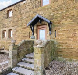 An exterior view of a stone house with steps leading to a wooden door at Winding Wheel Cottage in Cambois near Ashington