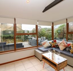A sunroom with a sofa with cushions and a wooden coffee table with wine glasses and a bottle at Winding Wheel Cottage in Cambois near Ashington