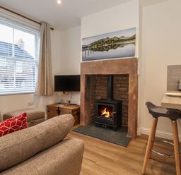 A living room with a fireplace a television and a kitchen bar stool at Jack's Cottage in Keswick