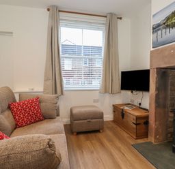 A living room with a sofa and red cushions a window with curtains a wood storage chest a mounted television and a fireplace at Jack's Cottage in Keswick