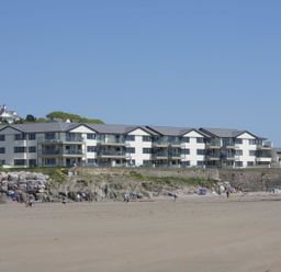 A beachfront modern apartment complex with balconies near a sandy beach with people at 19 Burgh Island Causeway in Bigbury-On-Sea