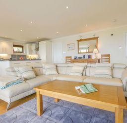 A living room with a beige sectional sofa a wooden coffee table and a kitchen area in the background at 19 Burgh Island Causeway in Bigbury-On-Sea