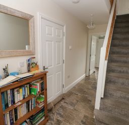 A hallway with a carpeted staircase a bookshelf a mirror and closed doors at Llygad Y Lleuad Moon in Burry Port