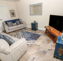 A living room with two beige sofas a TV on a wooden stand a blue side table and a blue patterned rug at Llygad Y Lleuad Moon in Burry Port