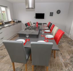 A kitchen with a long dining table and chairs in red black grey and cream with a built in gas stove and kitchen cabinets at Llygad Y Lleuad Moon in Burry Port