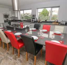 A kitchen with a long dining table with multicolored chairs set with plates and glasses at Llygad Y Lleuad Moon in Burry Port