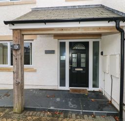 The entrance of a house with a black front door under a small roof supported by wooden posts at Llygad Yr Haul Sun in Burry Port