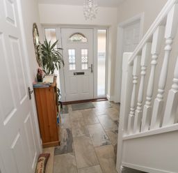 A hallway with a front door a wooden cabinet a plant a mirror and white staircase at Llygad Yr Haul Sun in Burry Port