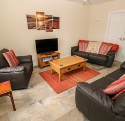 A living room with three black leather sofas a wooden coffee table and a television on a wooden stand at Llygad Yr Haul Sun in Burry Port