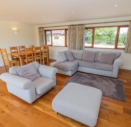 A living room with a grey sofa set and wooden dining table near windows at Little Owl Barn in Upton Snodsbury