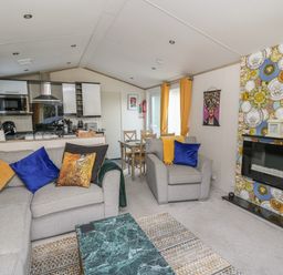 A living room with gray sofas and colorful pillows next to a kitchen and dining table at 95 Hafan Taffy in Gilfachrheda near Llanarth
