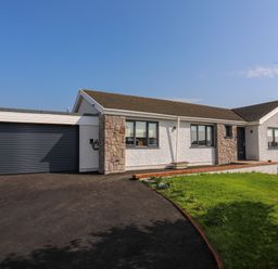 A single story house with a garage driveway and lawn at Corrie Knowe in Trearddur Bay