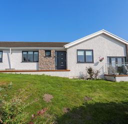 A single story house with white walls stone accents and a grass lawn at Corrie Knowe in Trearddur Bay
