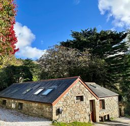 A stone cottage with skylight windows on a slate roof surrounded by trees at Harveys House in Helston
