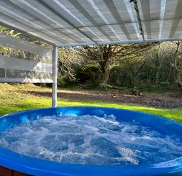 An outdoor hot tub with bubbling water under a striped canopy in a garden with trees at Harvey's House in Helston