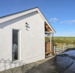 A white building exterior with a small porch and wooden railing next to a fenced area with a grassy field in the background at Capel Park (Tyddynod Bach) in Llandyfrydog near Llanerchymedd