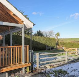 A covered wooden porch with railing overlooking a fenced garden with lawn and hedges at Capel Park (Tyddynod Bach) in Llandyfrydog near Llanerchymedd