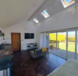 A living room with kitchen area dining table and sliding glass doors opening to a garden at Capel Park (Tyddynod Bach) in Llandyfrydog near Llanerchymedd