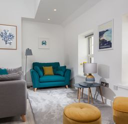 A living room with teal and gray sofas yellow poufs and coastal artwork at Chy Lowen in Porthleven