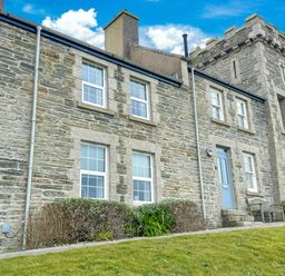 Stone building with multiple windows blue door bench and manicured lawn at Chy Lowen in Porthleven