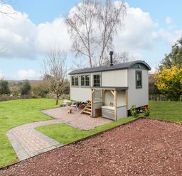 A small shed on wheels with stairs and outdoor seating on a paved area in a garden at Evendine Hut @ Evendine Cottage in Colwall Herefordshire